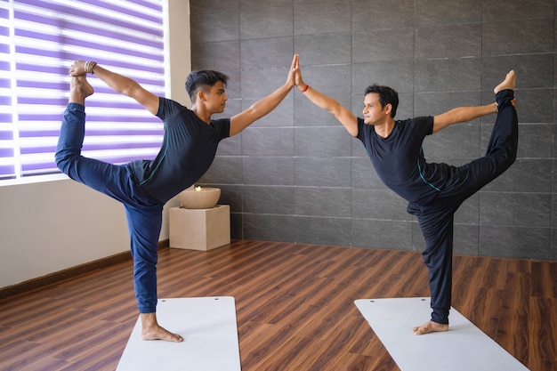 Two yogis doing lord of dancers pose in gym