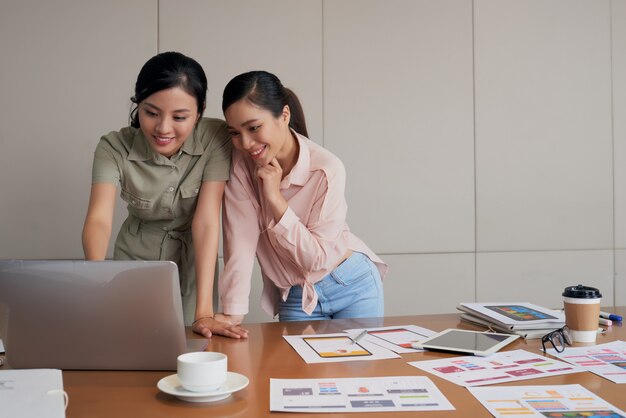 책상에 서서 노트북을 사용하는 두 젊은 아시아 여성 동료