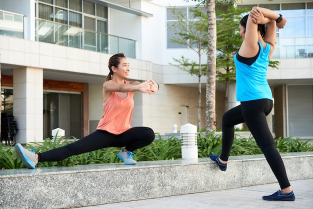 Two young Asian female joggers stretching in city street 