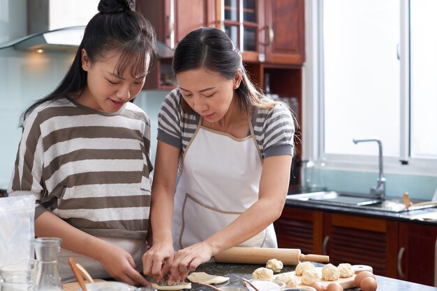 Две молодые азиатские женщины вырезали печенье из теста на кухонном столе
