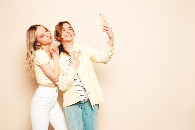 Two young beautiful blond smiling hipster female in trendy summer clothes