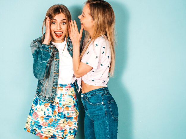 Две молодые красивые белокурые улыбающиеся хипстерские девочки в модной летней повседневной одежде.