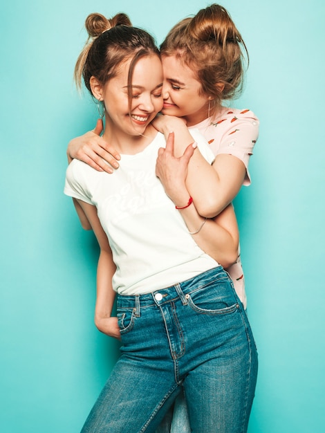 Two young beautiful blond smiling hipster girls in trendy summer hipster jeans clothes. sexy carefree women posing near blue wall. trendy and positive models having fun