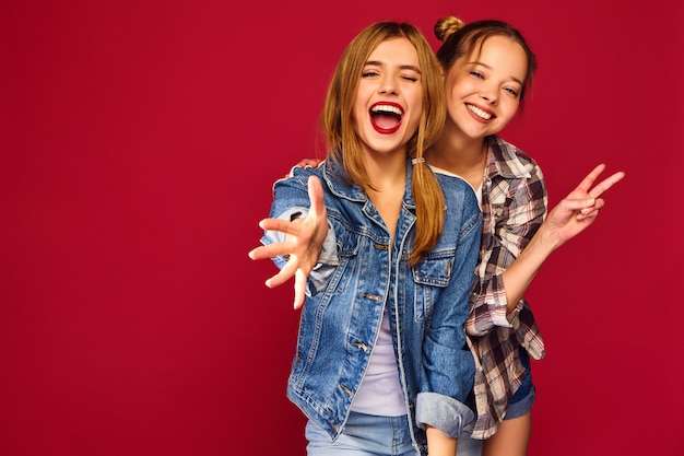 Две молодые красивые белокурые улыбающиеся женщины-хипстеры позируют в модной летней клетчатой рубашке