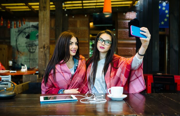Free Photo two young and beautiful girl sitting at the table and doing selfie in the cafe