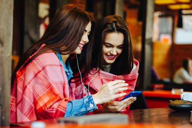 スマートフォンで音楽を聴いてテーブルに座っている2人の若くて美しい少女