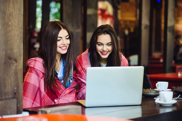 Two young and beautiful girl sitting at the table and looking for something on the Internet