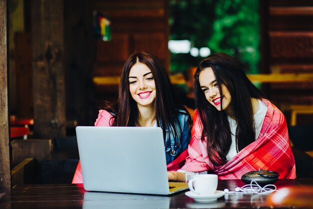 Two young and beautiful girl sitting at the table and looking for something on the Internet