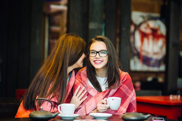 두 젊고 아름다운 소녀들이 커피 한 잔과 함께 테라스에서 수다를 떨고 있다