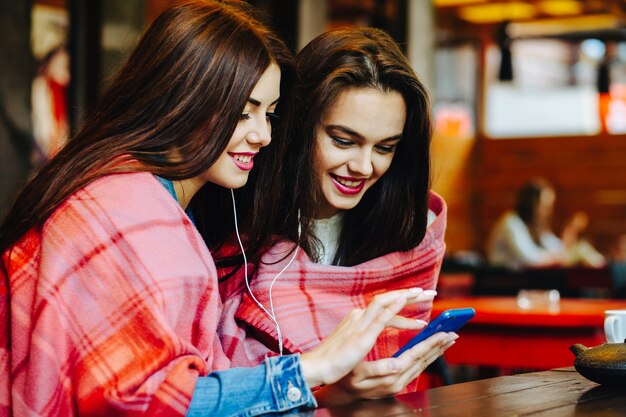 Two young and beautiful girls sitting at the table listening to music with a smartphone