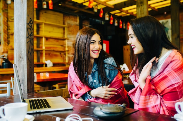 Two young and beautiful girls sitting at the table and looking for something on the internet