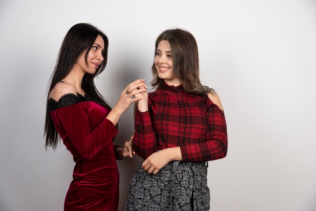 Two young beautiful girls standing and looking at each other on white wall .