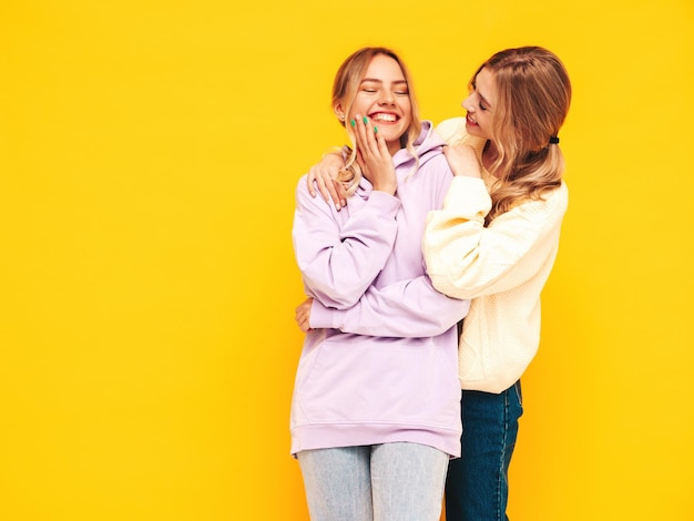 Two young beautiful smiling blond hipster female in trendy summer clothes Sexy carefree women posing near yellow wall in studio Positive models having fun Cheerful and happy