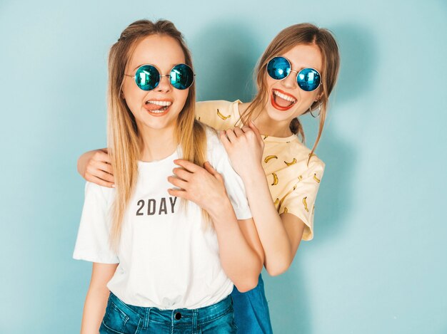 Two young beautiful smiling blond hipster girls in trendy summer colorful  clothes. 