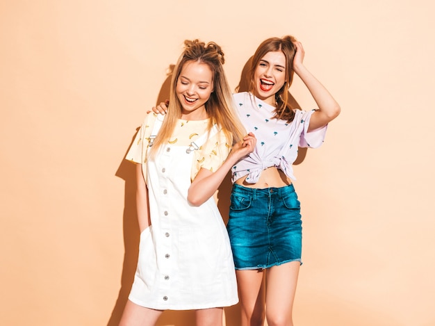 Free photo two young beautiful smiling blond hipster girls in trendy summer colorful t-shirt clothes. and showing tongue
