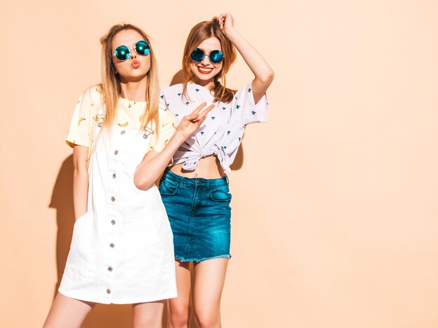 Две молодые красивые улыбающиеся белокурые хипстерские девочки в модной летней красочной футболке одеваются.