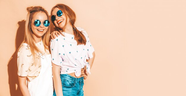 Две молодые красивые улыбающиеся белокурые хипстерские девочки в модной летней красочной футболке одеваются.