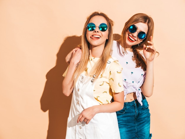 Two young beautiful smiling blond hipster girls in trendy summer colorful T-shirt clothes. 