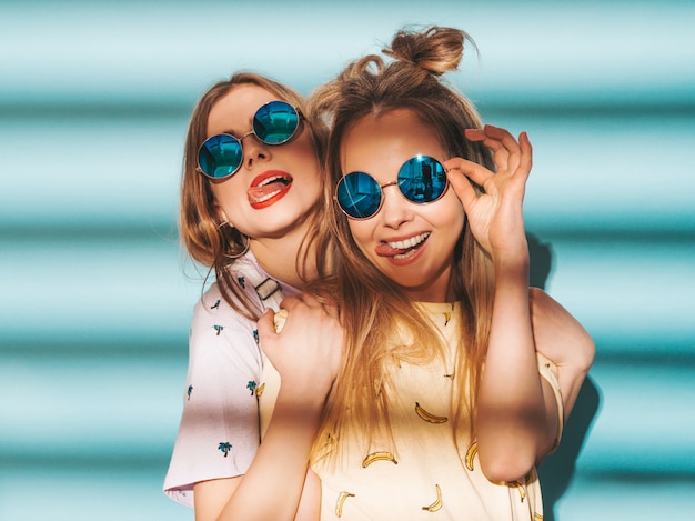 Foto gratuita due giovani belle ragazze bionde sorridenti dei pantaloni a vita bassa in vestiti variopinti della maglietta di estate alla moda.