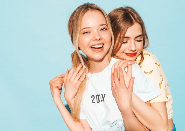 Two young beautiful smiling blond hipster girls in trendy summer colorful T-shirt clothes. 