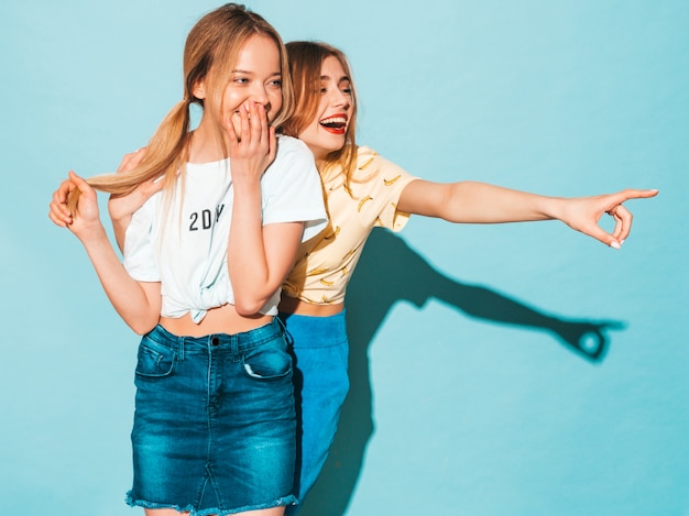 Two young beautiful smiling blond hipster girls in trendy summer colorful T-shirt clothes. 