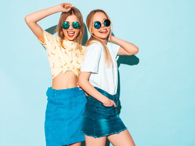 Две молодые красивые улыбающиеся блондинка битник девушки в модных летних джинсах юбки одежды. и показывая знак мира