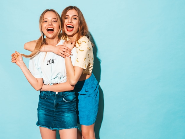 Two young beautiful smiling blond hipster girls in trendy summer jeans skirts clothes. 