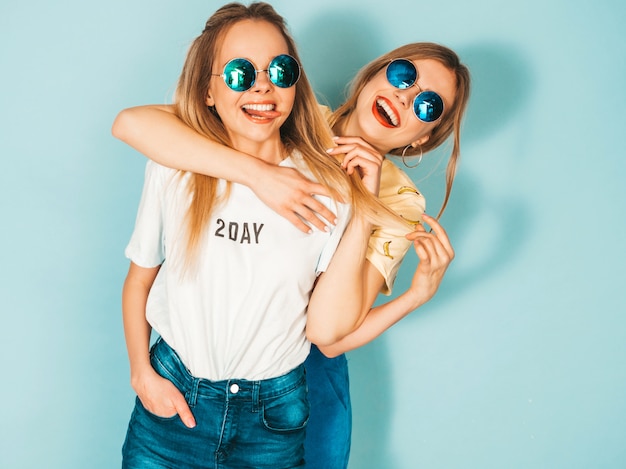 Two young beautiful smiling blond hipster girls in trendy summer jeans skirts clothes.