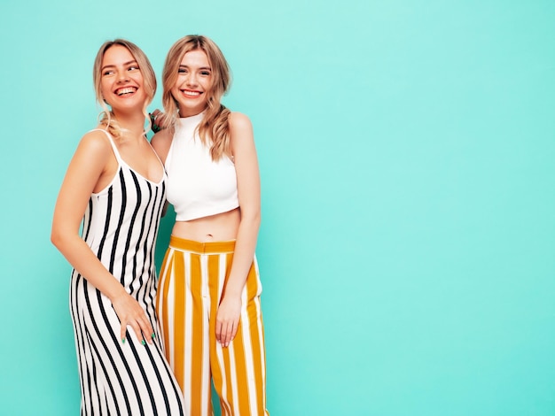 Two young beautiful smiling brunette hipster female in trendy summer clothes Sexy carefree women posing near blue wall in studio Positive models having fun Cheerful and happy