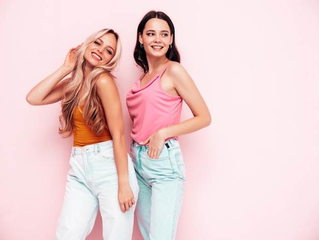 Две молодые красивые улыбающиеся брюнетки-хипстеры в модной летней одежде Сексуальные беззаботные женщины позируют возле розовой стены Позитивные модели веселятся Веселые и счастливые
