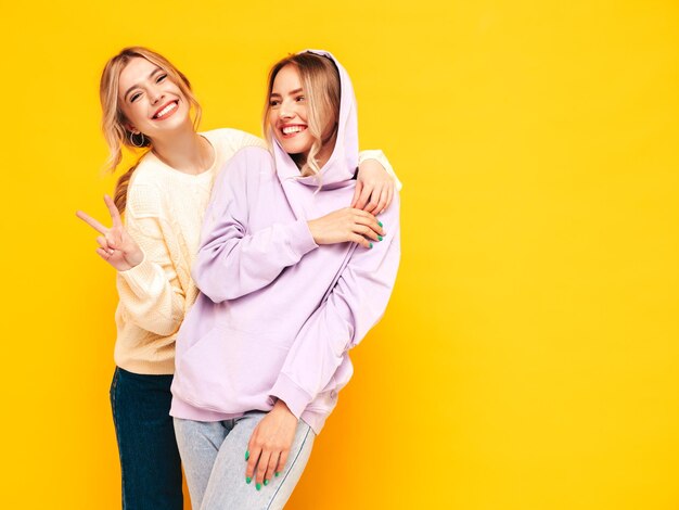 Two young beautiful smiling brunette hipster female in trendy summer clothes Sexy carefree women posing near yellow wall in studio Positive models having fun Cheerful and happy