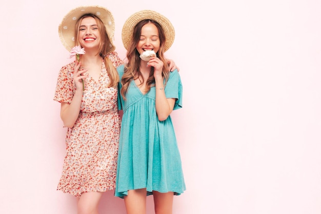 トレンディな夏のドレスを着た2人の若い美しい笑顔のブルネットのヒップスターの女性ピンクの壁の近くでポーズをとるセクシーな屈託のない女性
