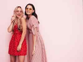 Free photo two young beautiful smiling brunette hipster female in trendy summer dresses sexy carefree women posing near pink wall positive models having fun cheerful and happy