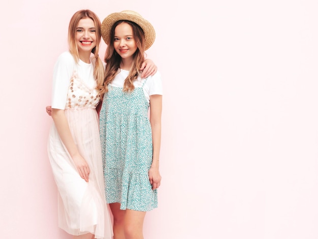 Two young beautiful smiling brunette hipster female in trendy summer dresses Sexy carefree women posing near pink wall Positive models having fun Cheerful and happy