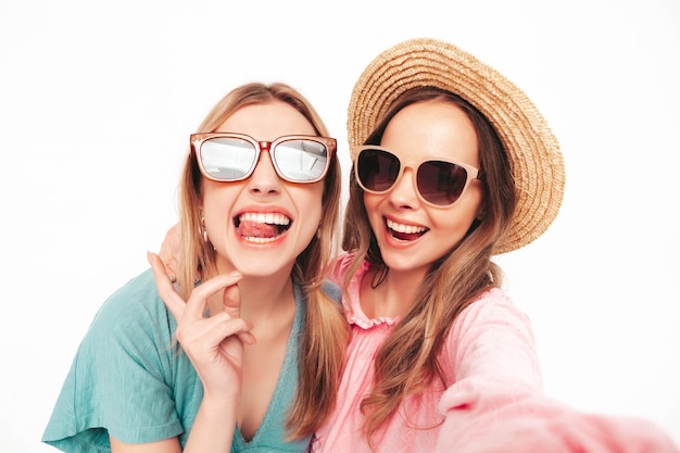 Two young beautiful smiling brunette hipster female in trendy summer dresses Sexy carefree women posing near white wall Positive models having fun Cheerful and happy Taking Pov selfie photos