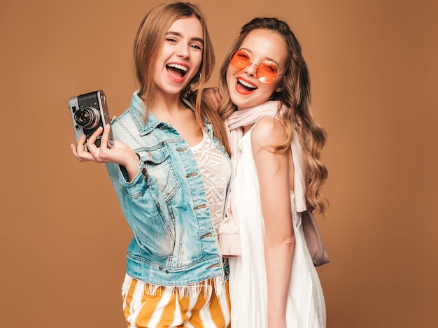 Две молодые красивые улыбающиеся девушки в модной летней повседневной одежды и солнцезащитные очки. Сексуальные беззаботные женщины позируют. Фотографировать на ретро камеру