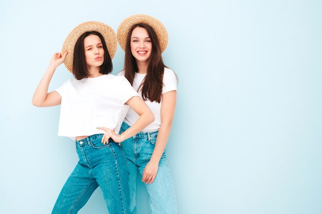 Две молодые красивые улыбающиеся хипстерские девушки в модной той же летней белой футболке и джинсовой одежде