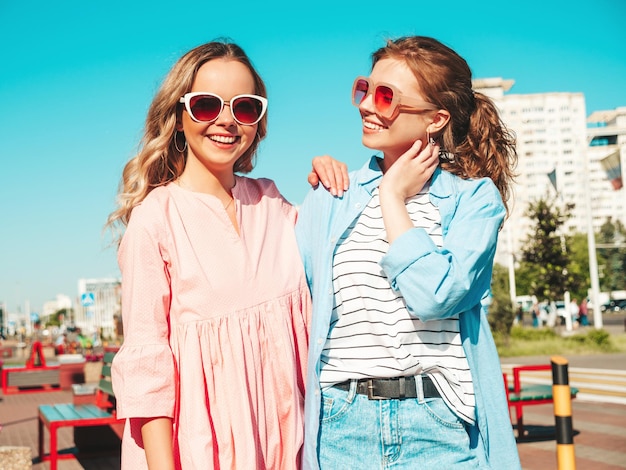 Due giovani belle donne hipster sorridenti in abiti estivi alla moda e vestito donne spensierate sexy in posa sullo sfondo della strada modelli puri positivi che si divertono al tramonto abbracciandosi e impazzendo