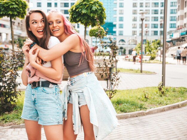 Two young beautiful smiling hipster female in trendy summer clothes.Sexy carefree women posing in the street with pink hair. Positive pure models having fun at sunset. Cheerful and happy