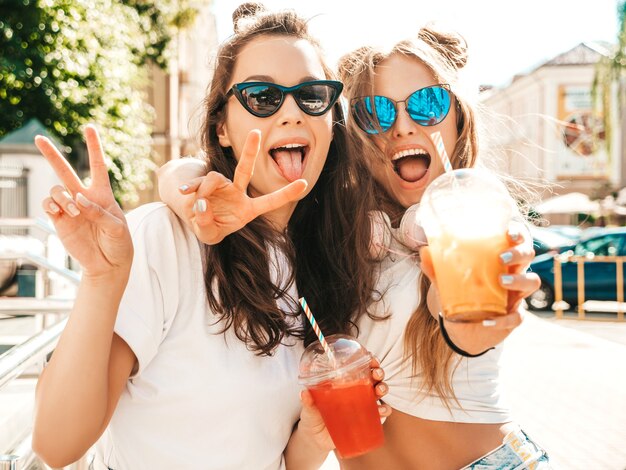 Two young beautiful smiling hipster female in trendy summer clothes
