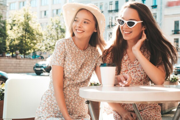 トレンディな夏の服を着た2人の若い美しい笑顔のヒップスターの女性ベランダカフェでおしゃべりし、お茶やコーヒーを飲むのんきな女性
