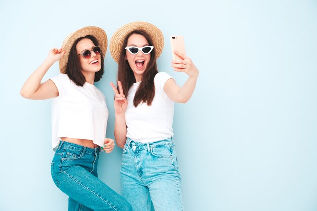 Due giovani belle donne hipster sorridenti in t-shirt bianca estiva alla moda e vestiti di jeans