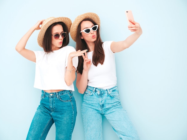 トレンディな夏の白いTシャツとジーンズの服を着た2人の若い美しい笑顔の流行に敏感な女性