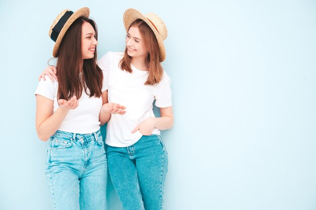 Две молодые красивые улыбающиеся хипстерские девушки в модной летней белой футболке и джинсовой одежде
