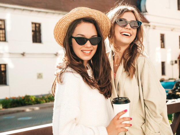 Две молодые красивые улыбающиеся хипстерские девушки в модном белом свитере и пальто