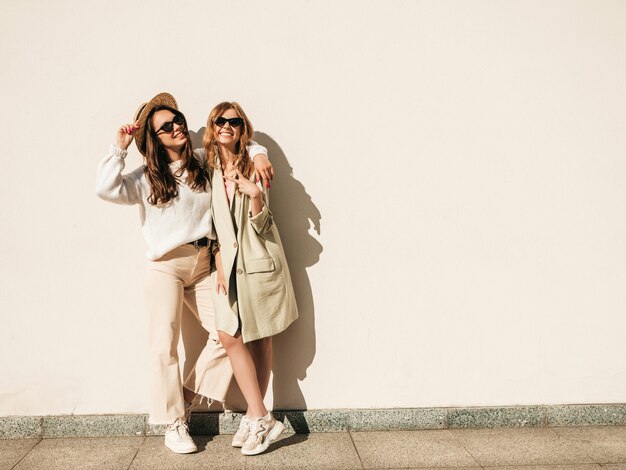 Two young beautiful smiling hipster female in trendy white sweater and coat