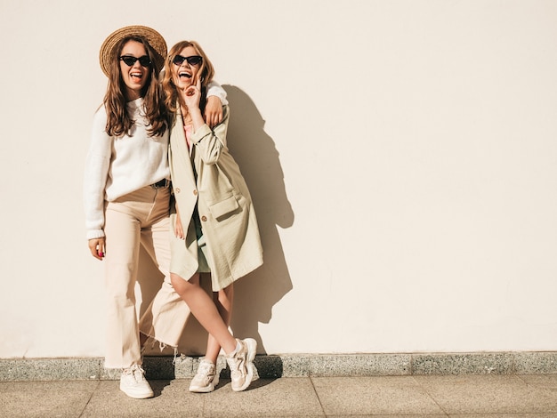 Two young beautiful smiling hipster female in trendy white sweater and coat