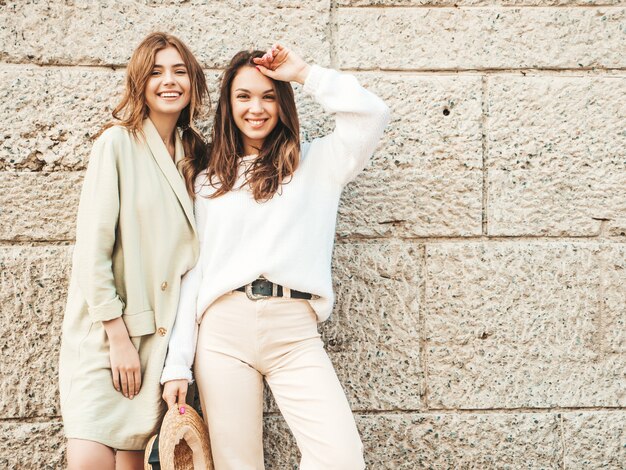 Two young beautiful smiling hipster female in trendy white sweater and coat