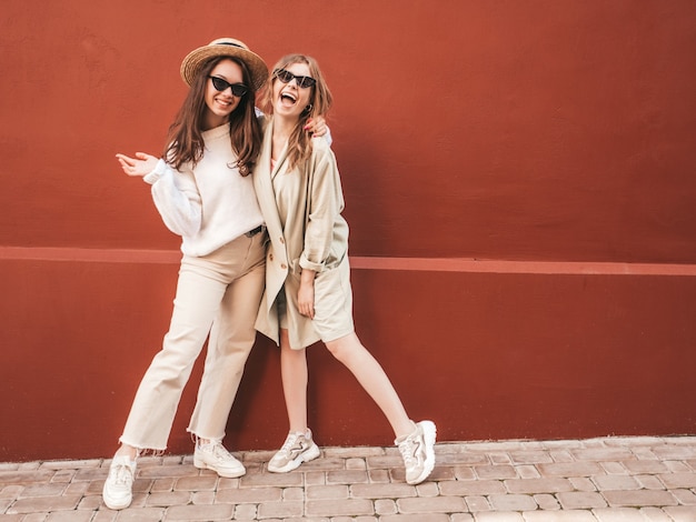 트렌디한 흰색 스웨터와 코트를 입은 두 젊은 아름다운 웃는 힙스터 여성