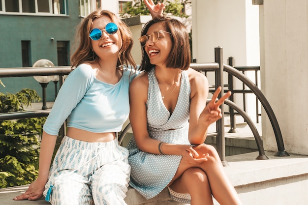 무료 사진 유행 여름 옷에 두 젊은 아름 다운 웃는 hipster 여자. 선글라스에 거리 배경에 포즈 섹시 평온한 여자. 재미 있고 미쳐가는 긍정적 인 모델